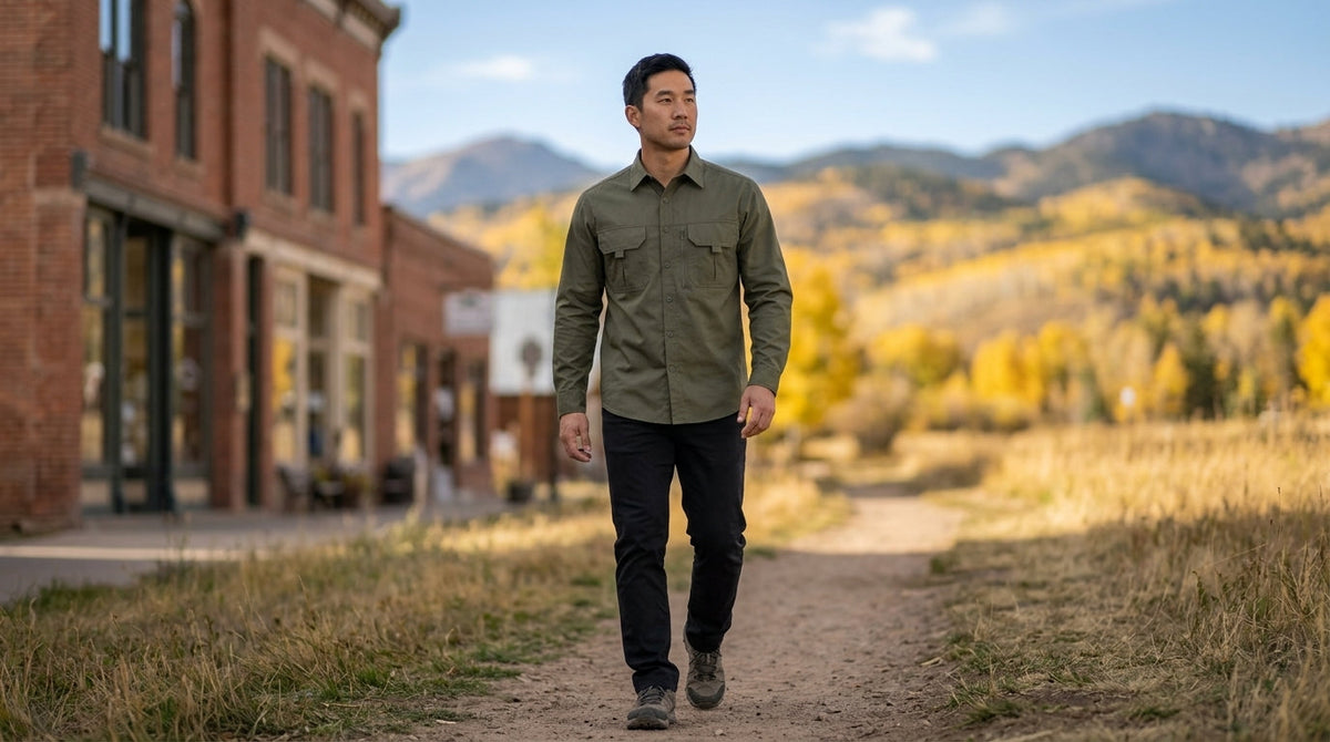 Man in an army green utility work shirt walking from a Colorado small-town street onto a trail in fall