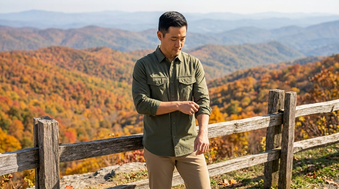 Man rolling the sleeves of an olive green long-sleeve work shirt at a Blue Ridge overlook in fall