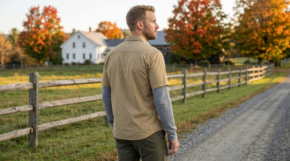 Man wearing a khaki short-sleeve button-up shirt over a gray long-sleeve thermal on a Vermont country road in fall