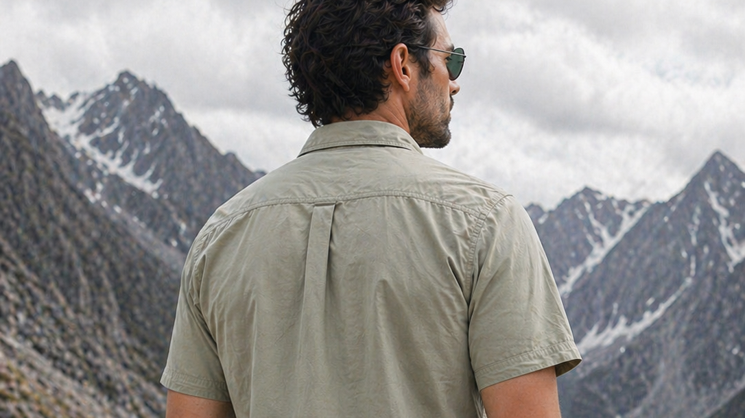 Man in a sage military-style cotton shirt looking out at snowy mountain peaks